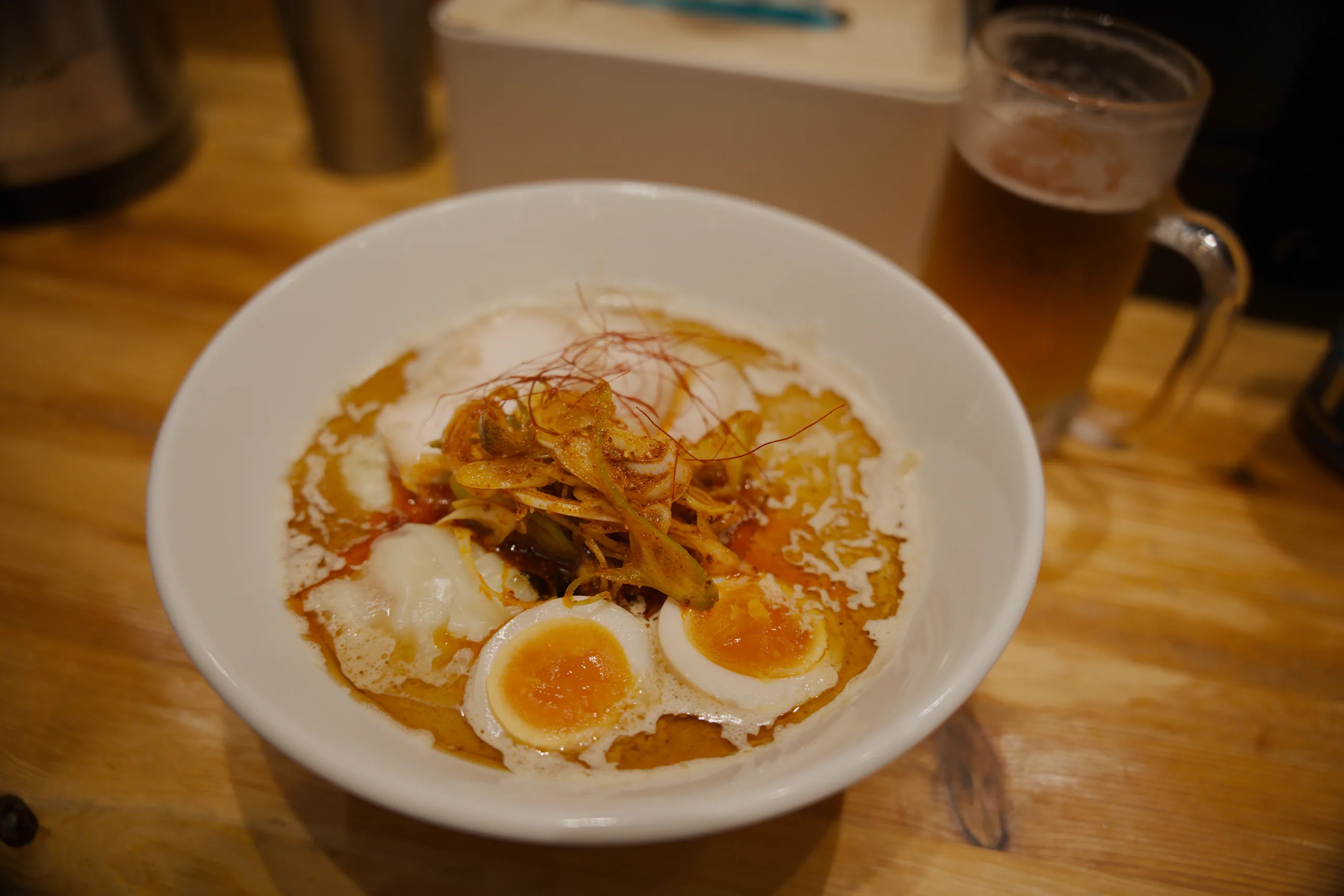 A bowl of ramen with soft-boiled eggs and crispy noodle topping on a wooden table.