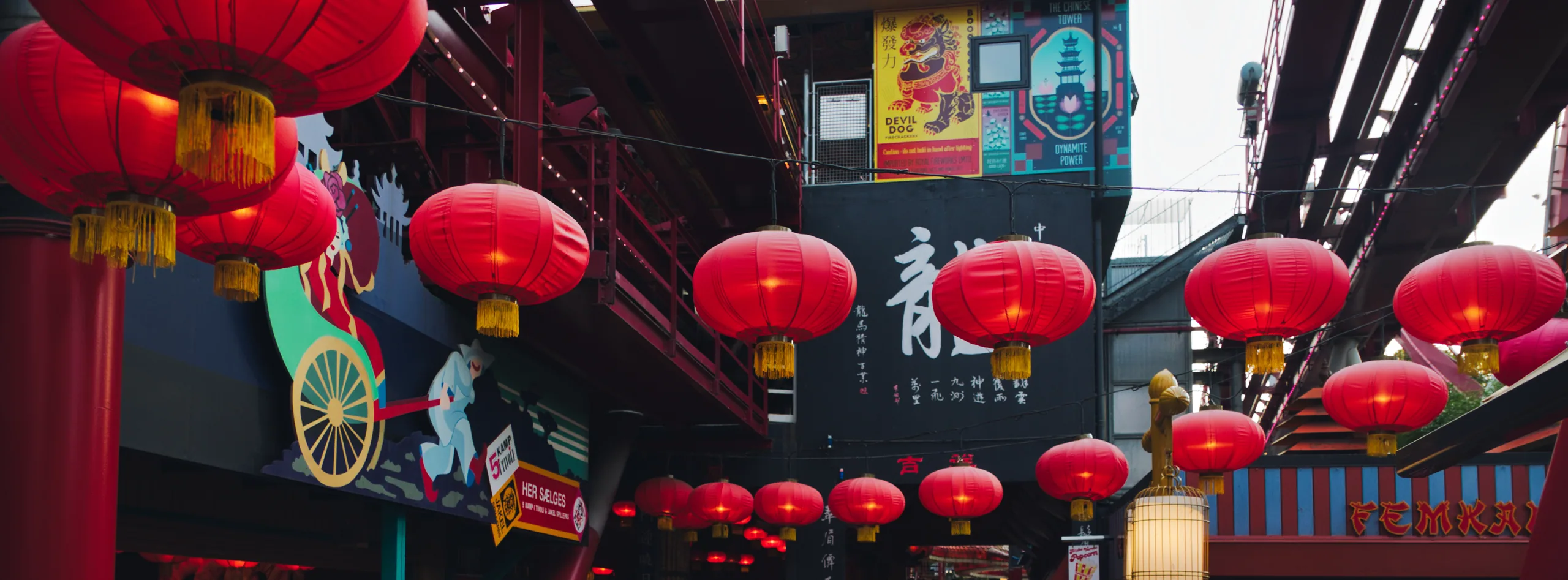 Rows of red Chinese lanterns strung beneath a ride at Tivoli, with dragon signage and painted panels behind.