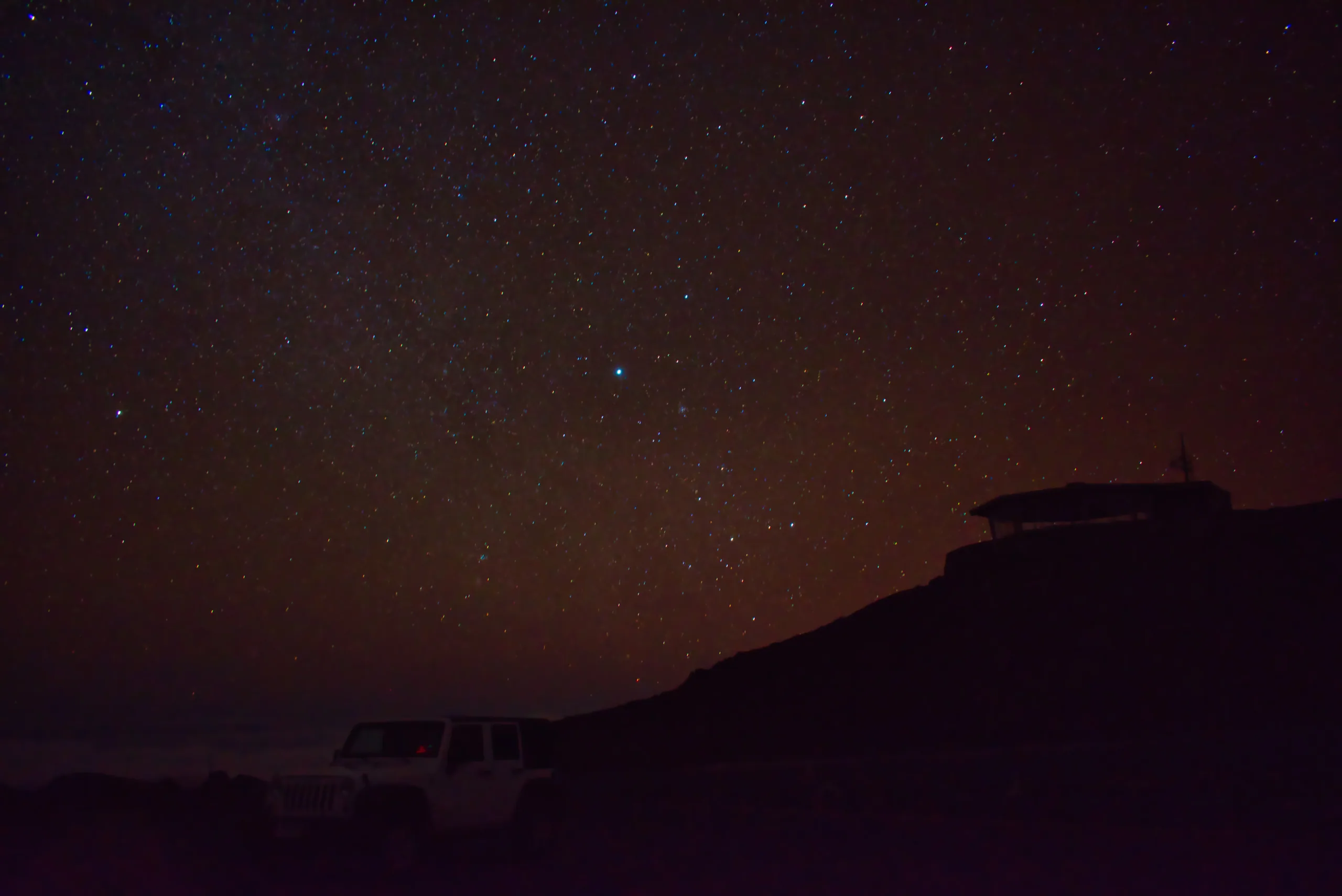 A parked truck silhouetted under a dense field of stars, the horizon a faint dark ridge.