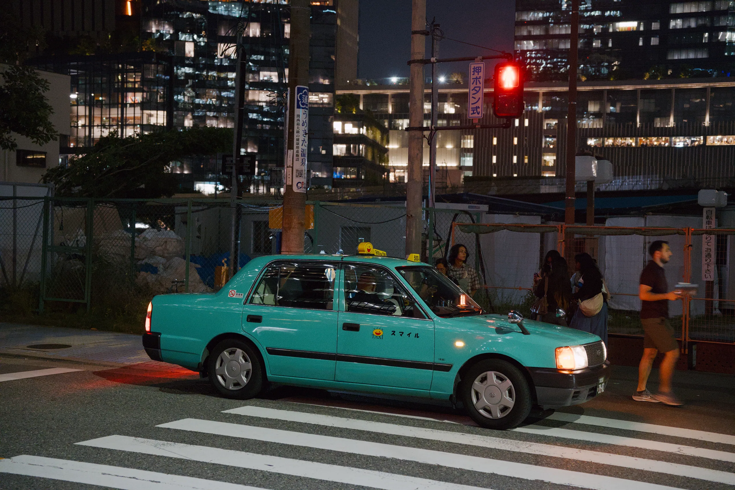 A turquoise taxi crosses a pedestrian crossing at night.