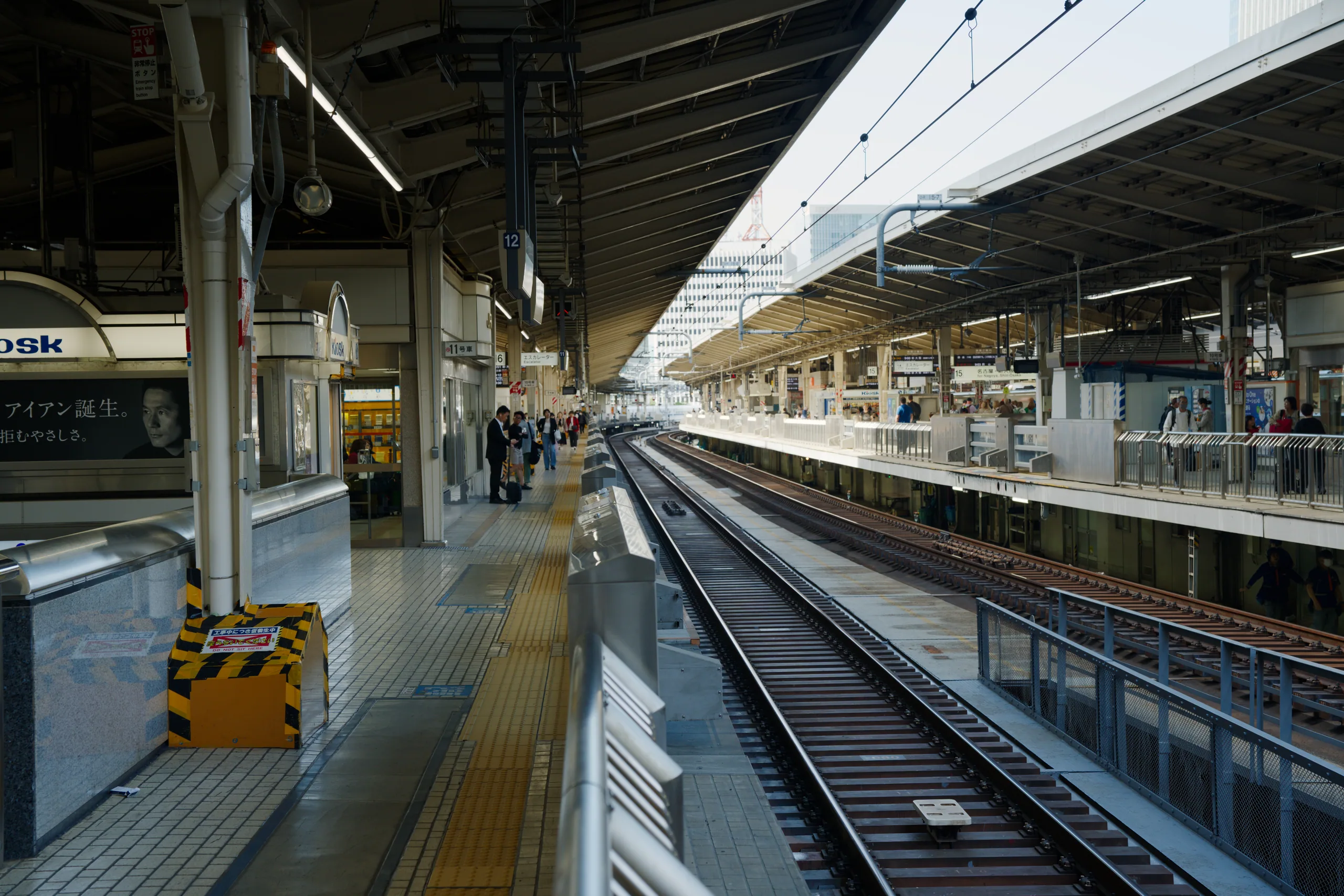 White bullet trains are parked at a train station platform beneath a glass roof and steel industrial infrastructure.
