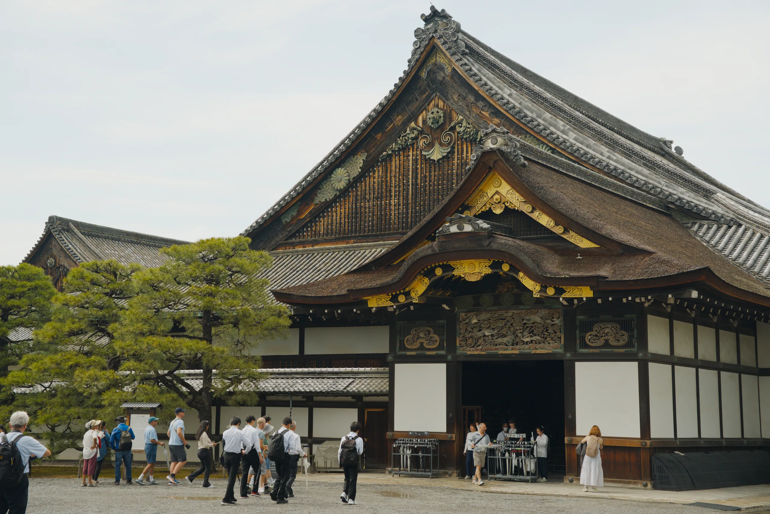 Temple courtyard with visitors gathered before a wooden building with black and gold facade.