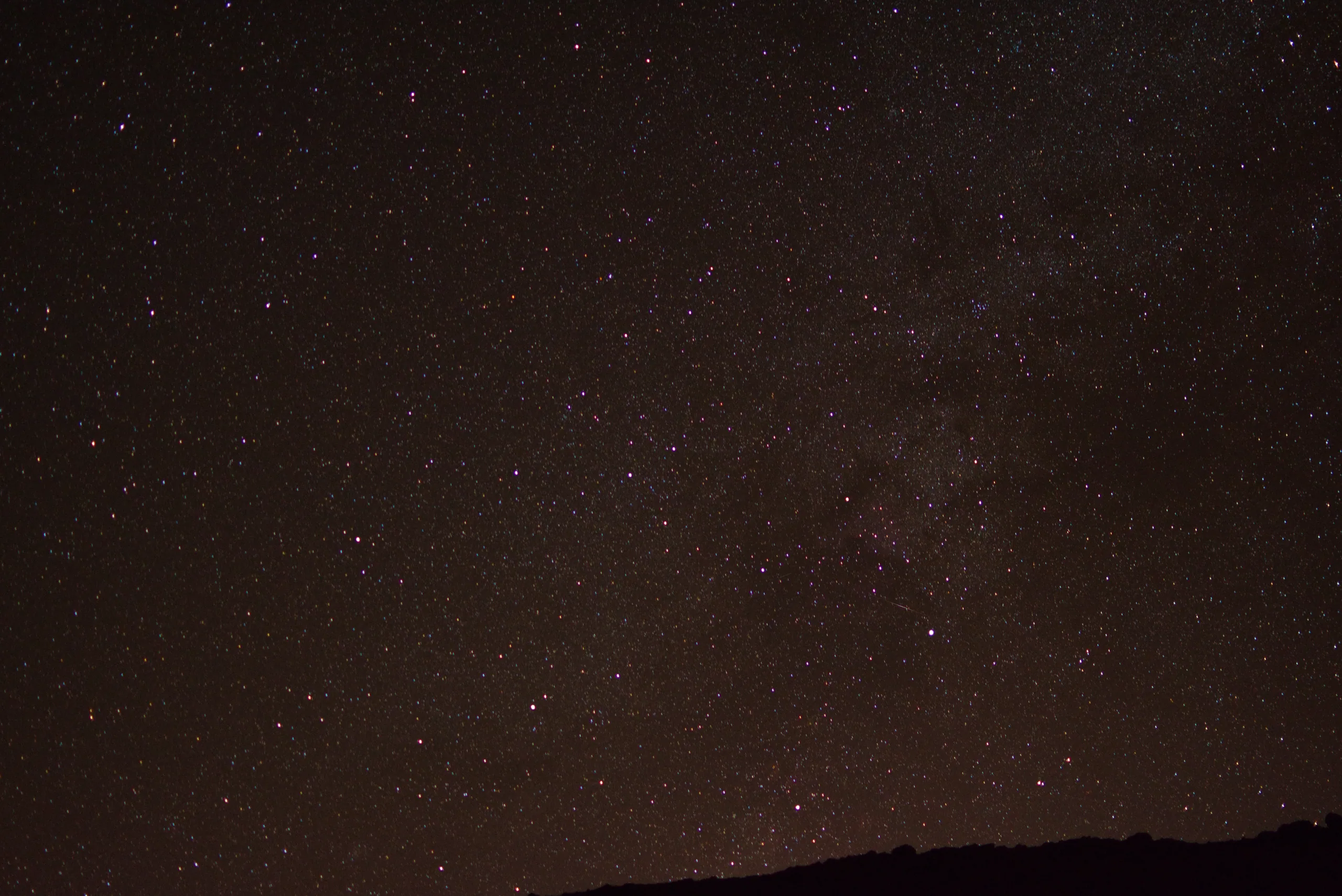 A dense star field filling the frame above a black horizon, the Milky Way faintly visible.
