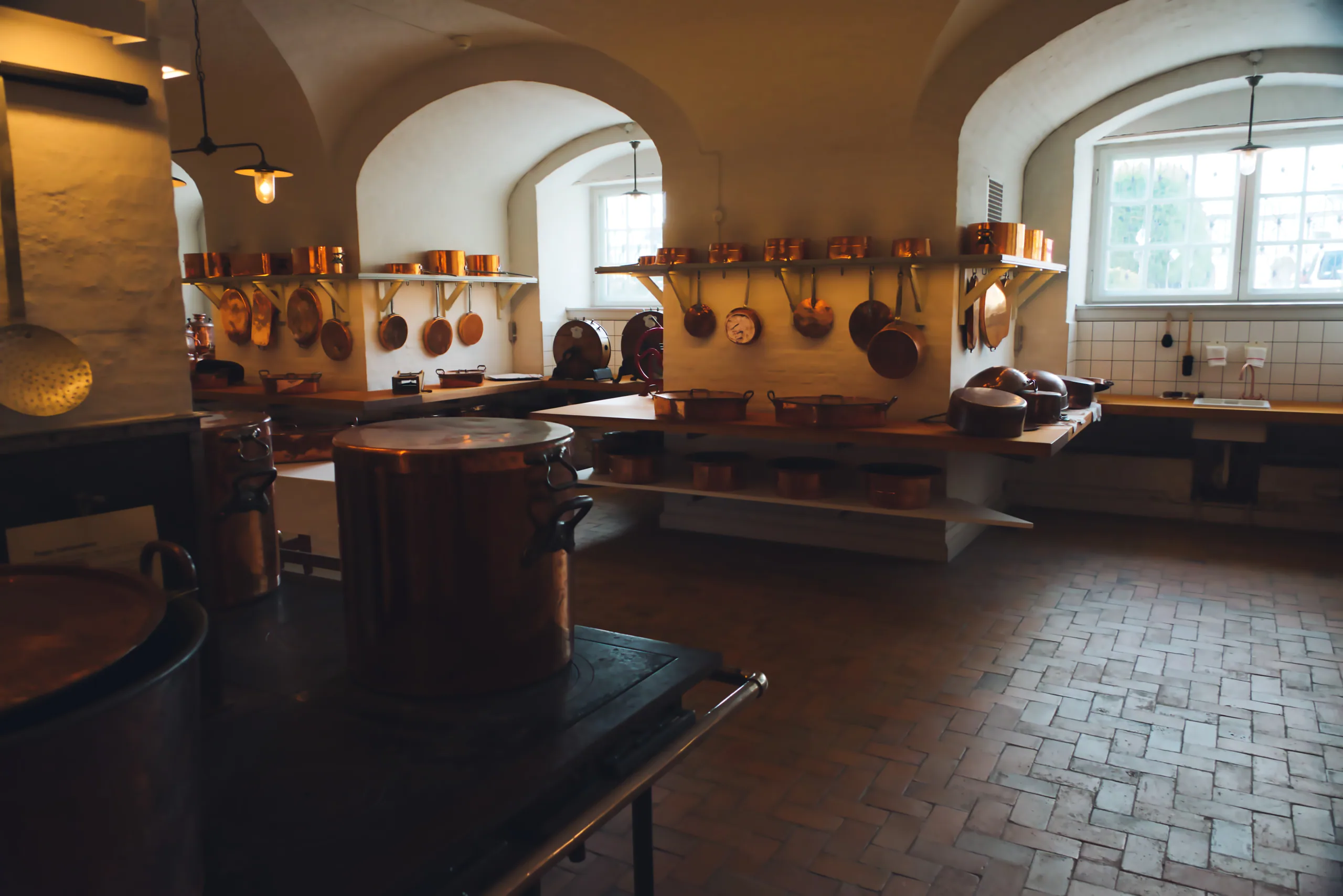 A historic palace kitchen with whitewashed vaulted ceilings, rows of copper pans on the walls and a flagstone floor.