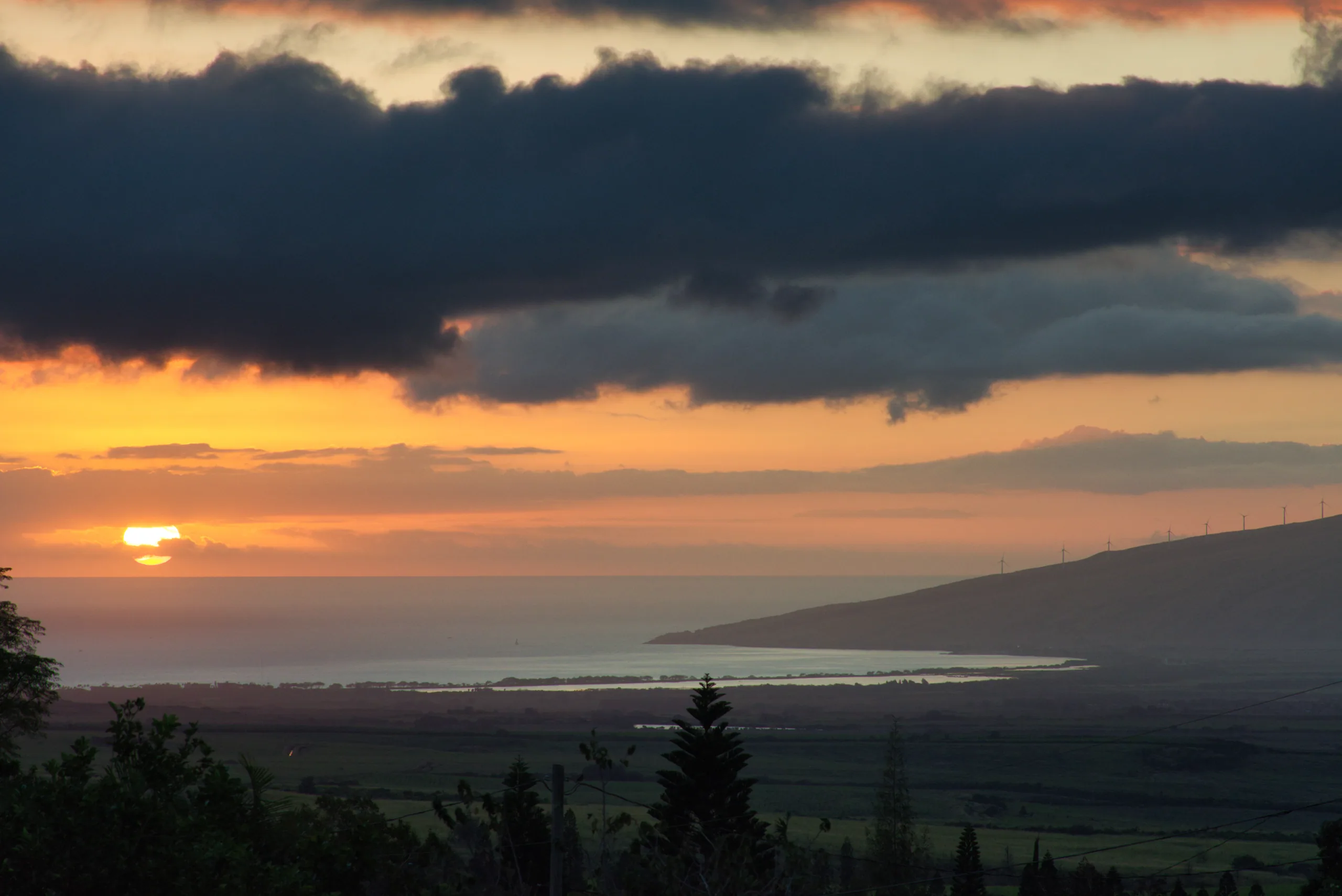 The sun setting into a bank of dark cloud over a wide coastal plain, the sky orange along the horizon.