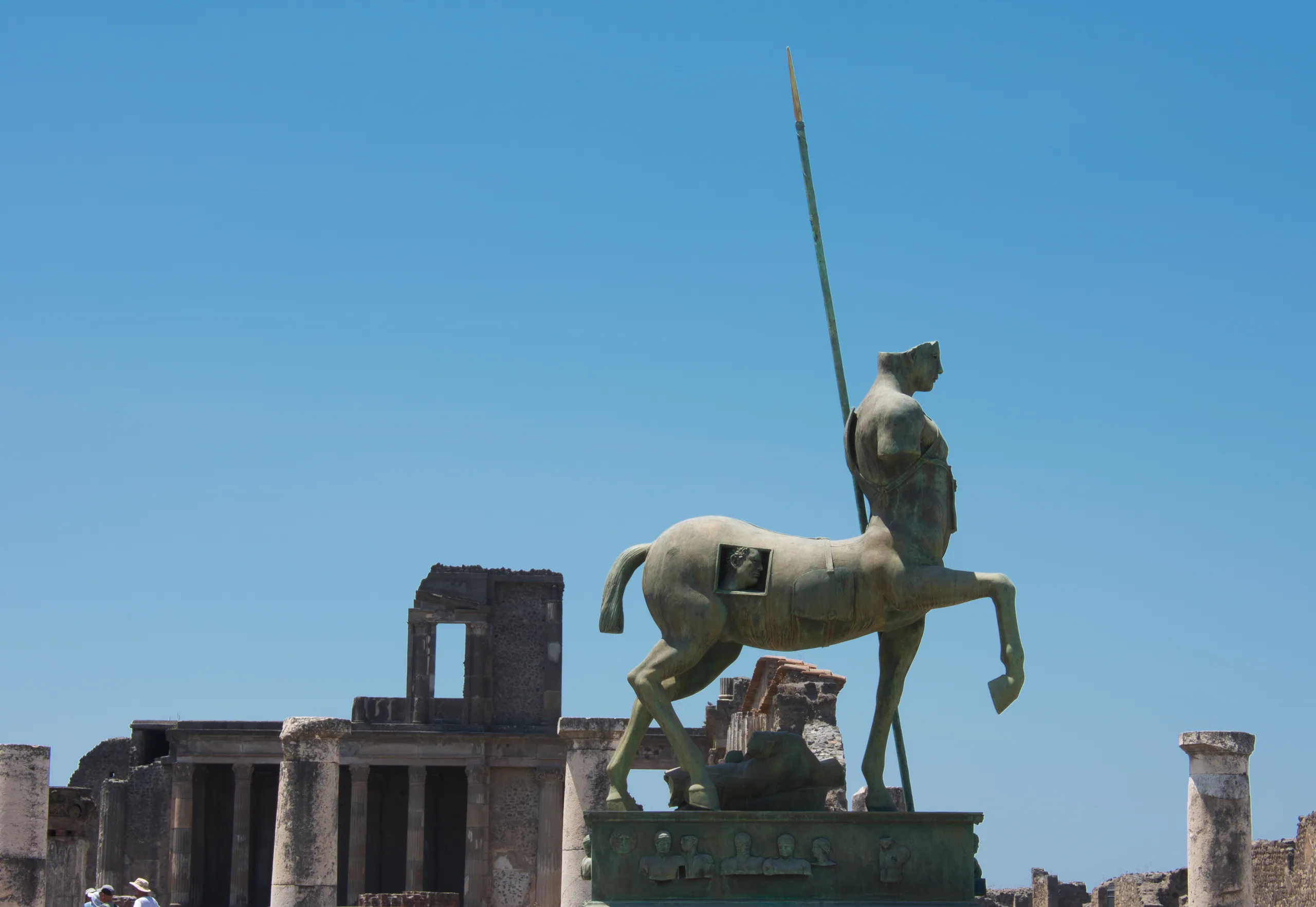 A bronze centaur sculpture with a raised spear standing among the excavated ruins of Pompeii.