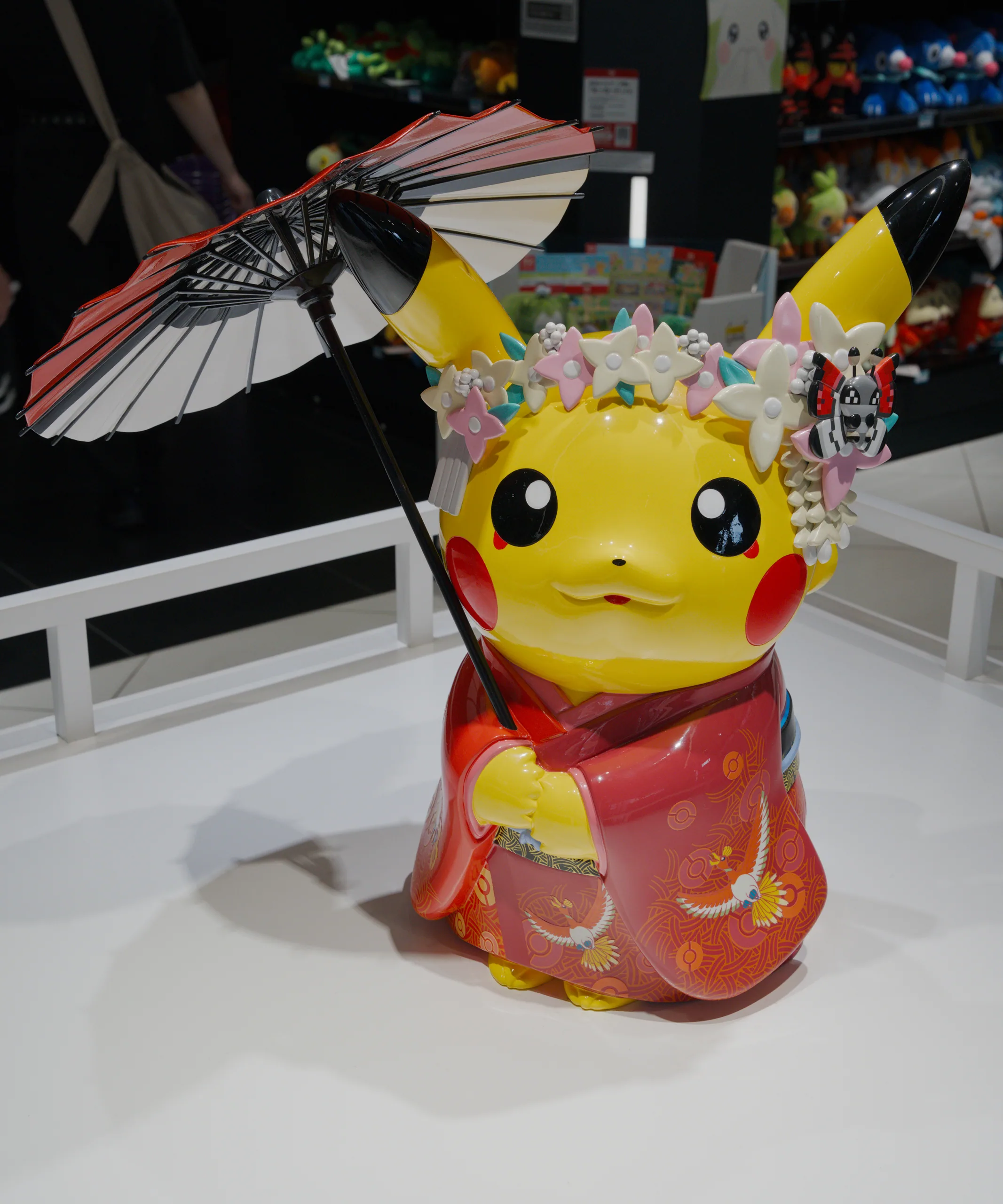 A yellow Pikachu figurine in a red outfit holds a small parasol among collectibles on display.