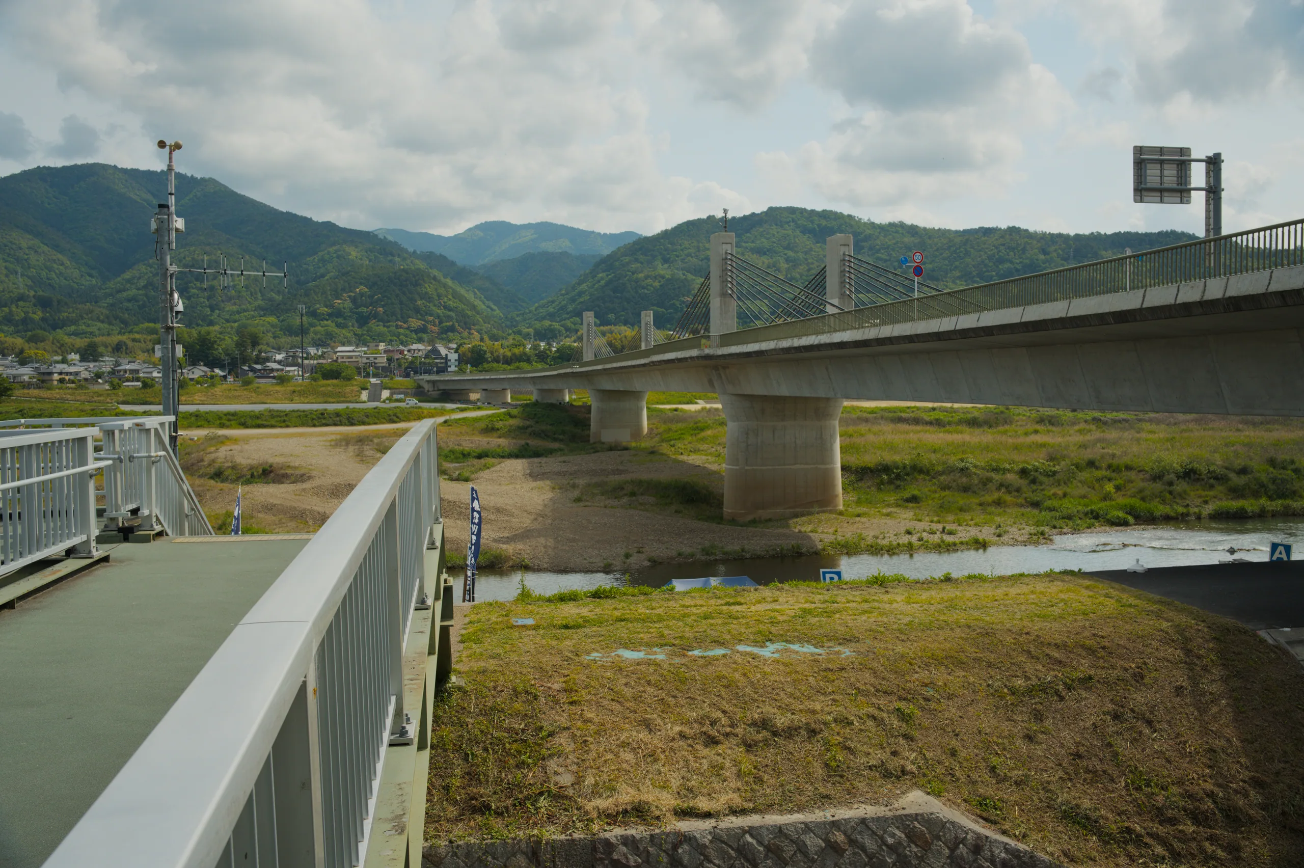 Looking across a river valley, a modern concrete bridge connects the banks with mountains rising beyond.