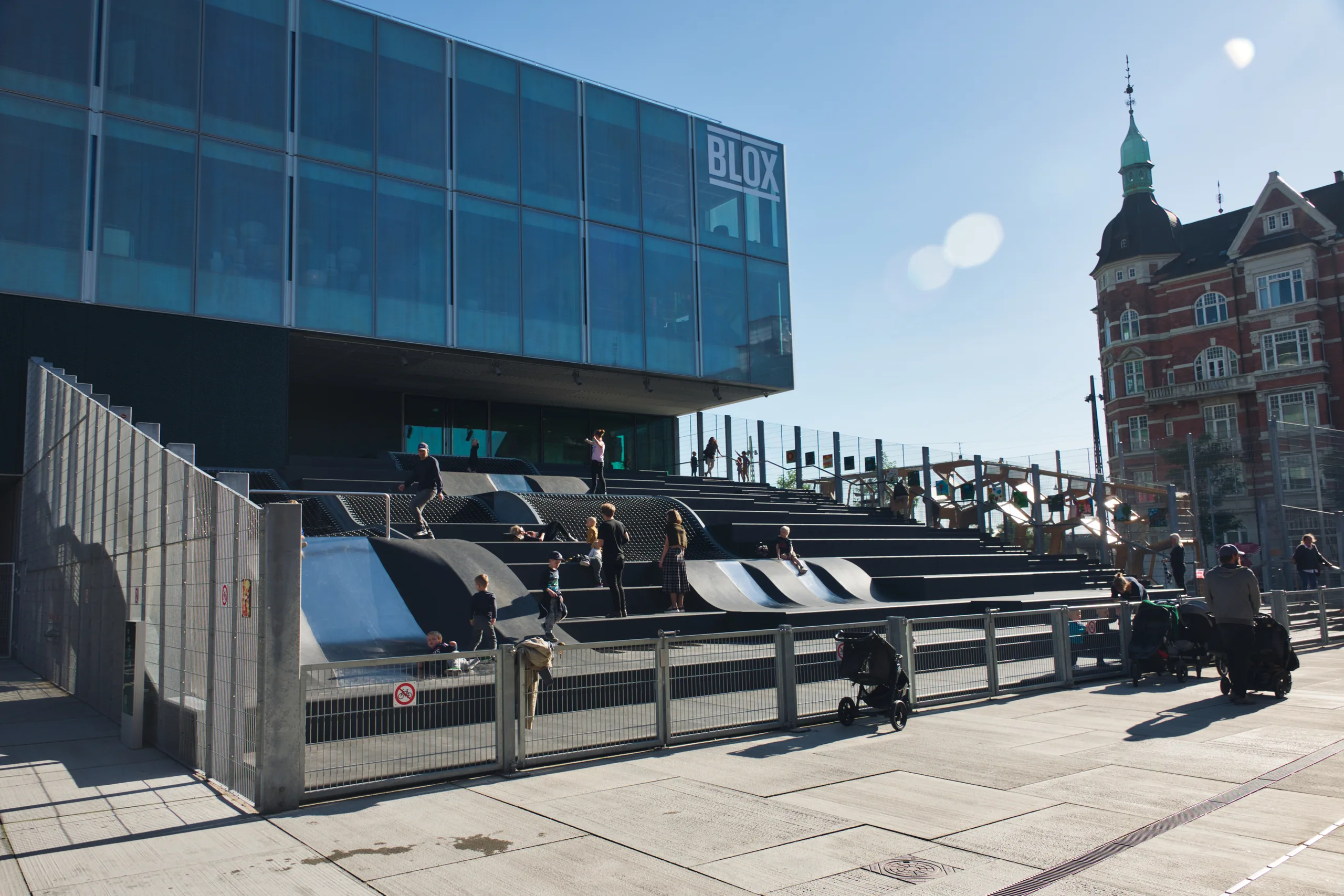 The BLOX building on the Copenhagen waterfront, a glass and dark-panelled block above a flight of wide public steps where people are sitting.