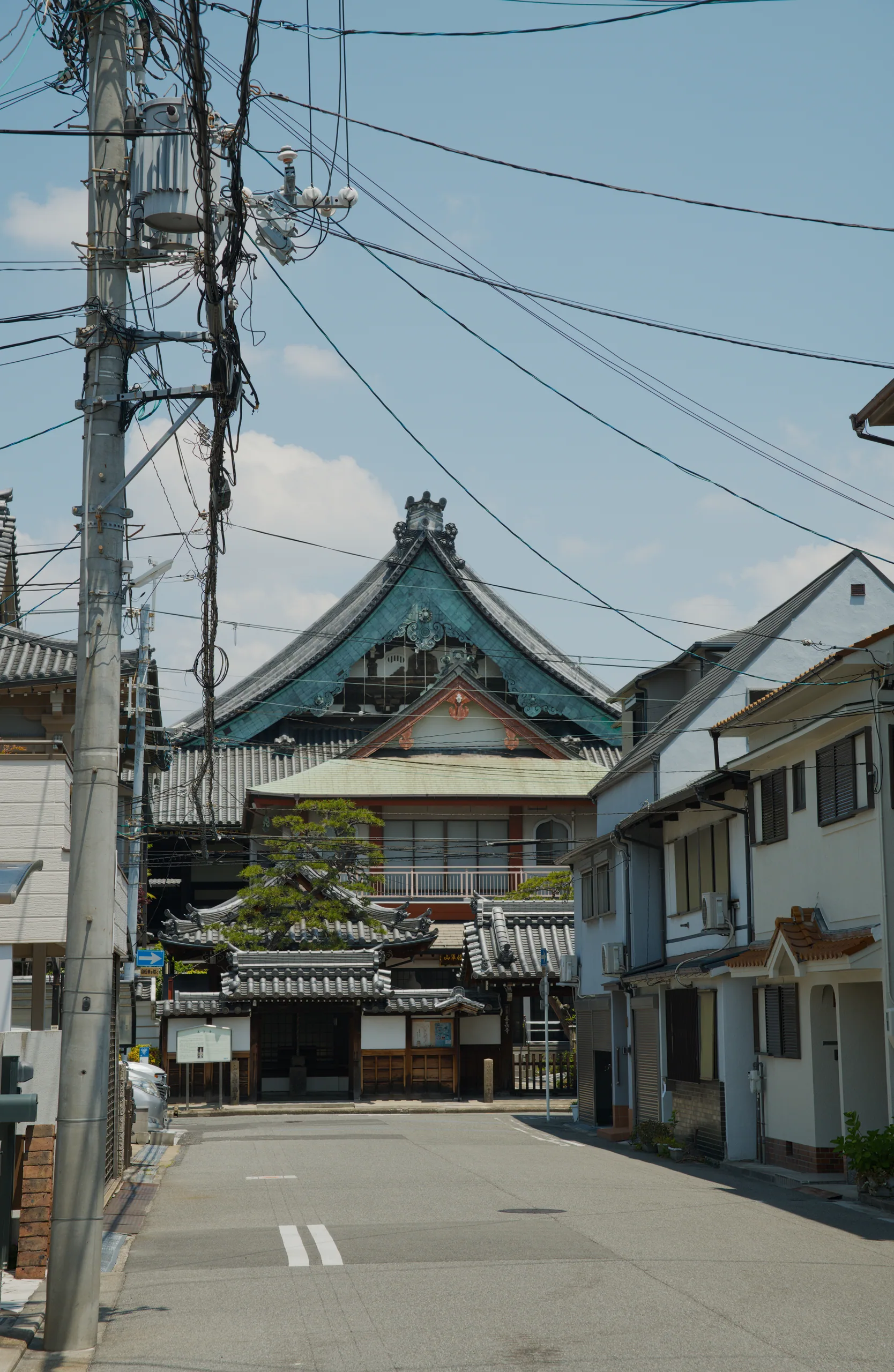 A traditional Japanese shrine entrance with characteristic architectural features stands beneath overhead power lines.