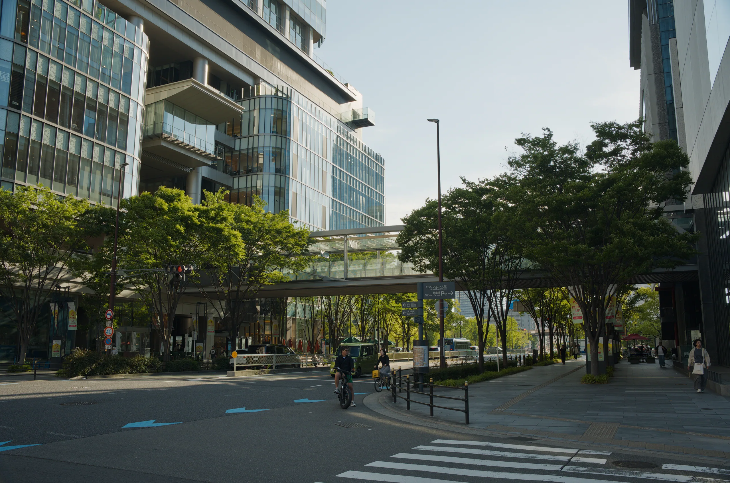 Public plaza with mature shade trees, paved walkway, and surrounding office buildings.