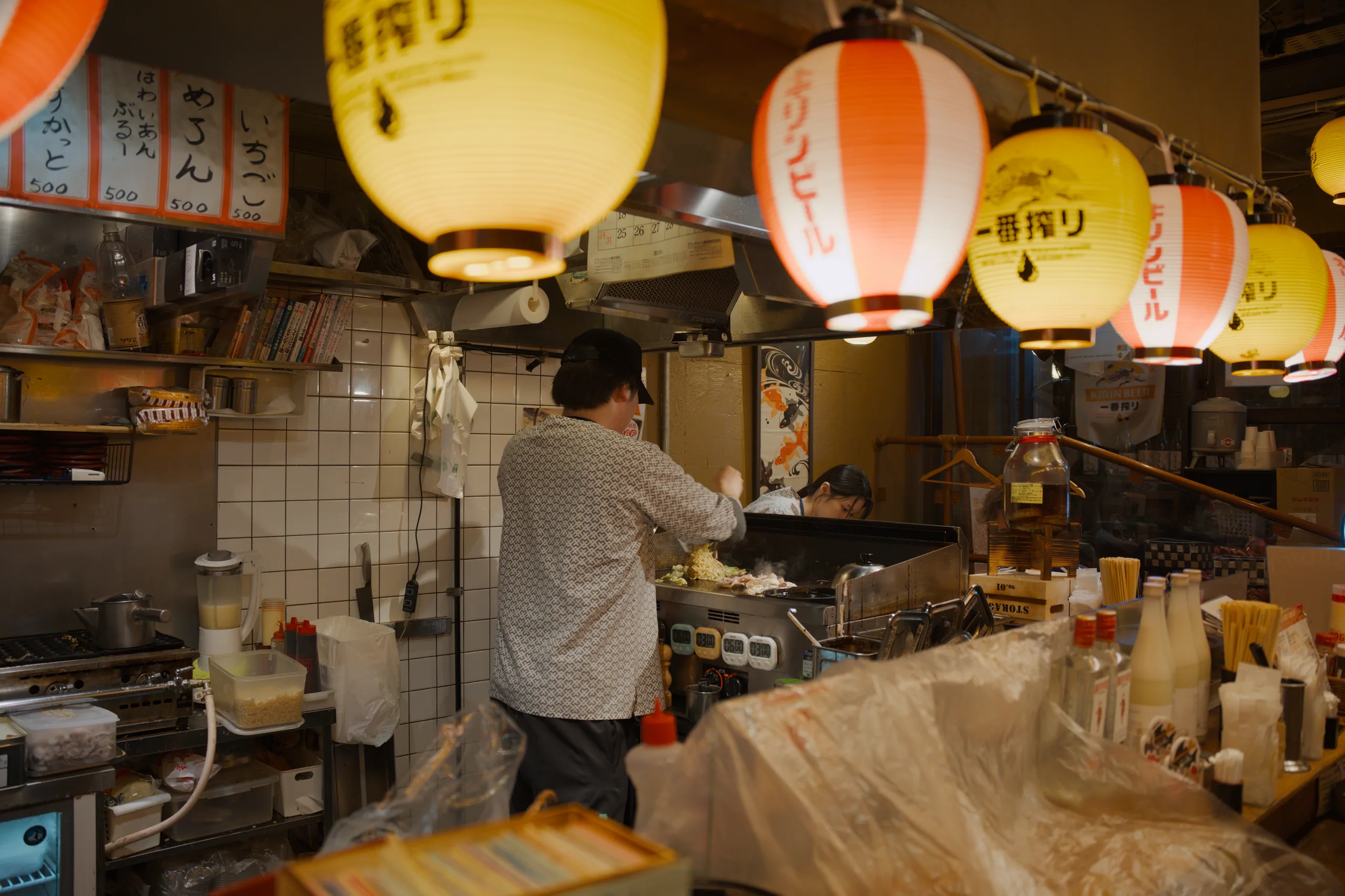 Izakaya interior with hanging paper lanterns and staff working at the counter.