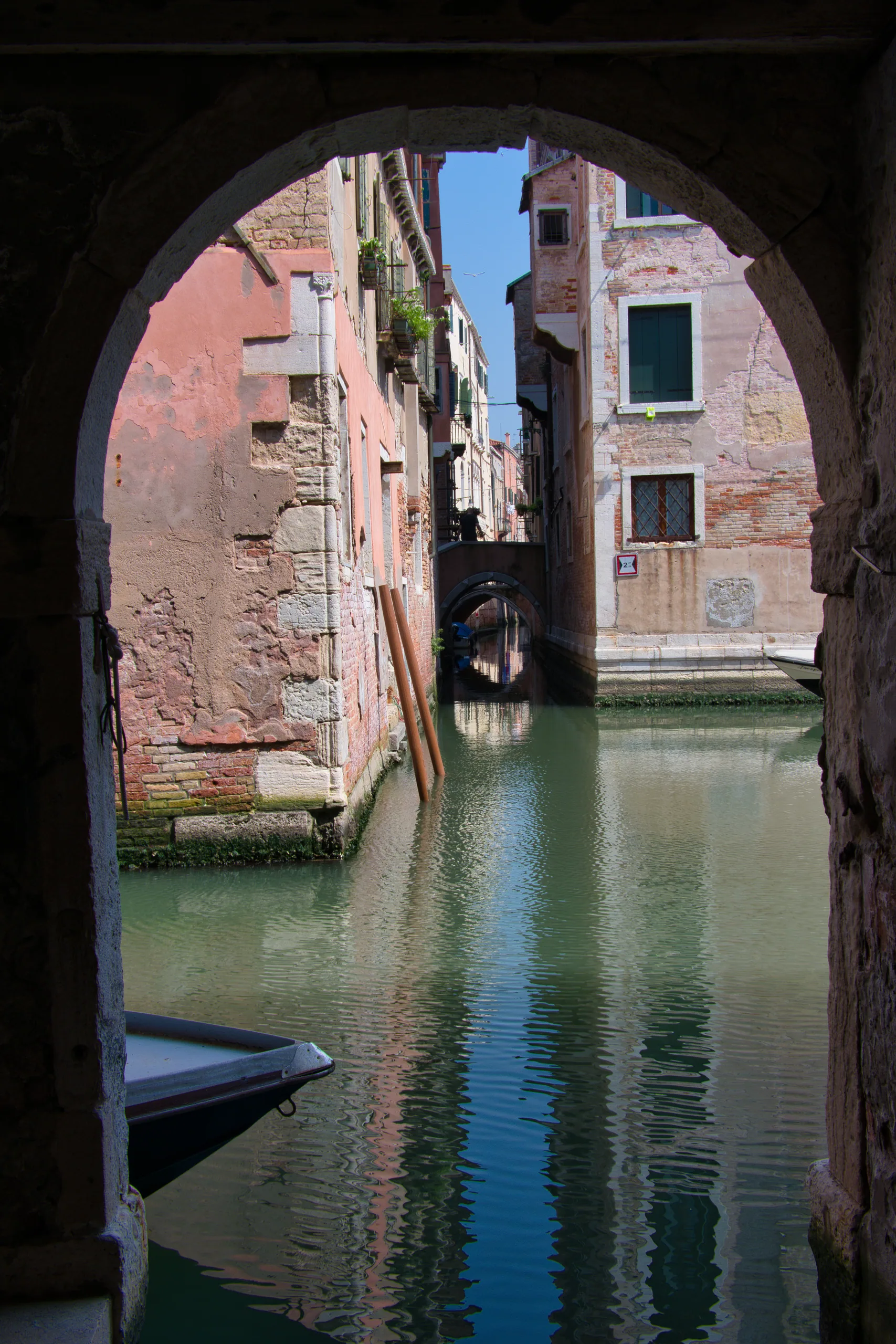 A canal in Venice seen through a stone archway, a further bridge visible down the waterway beyond.