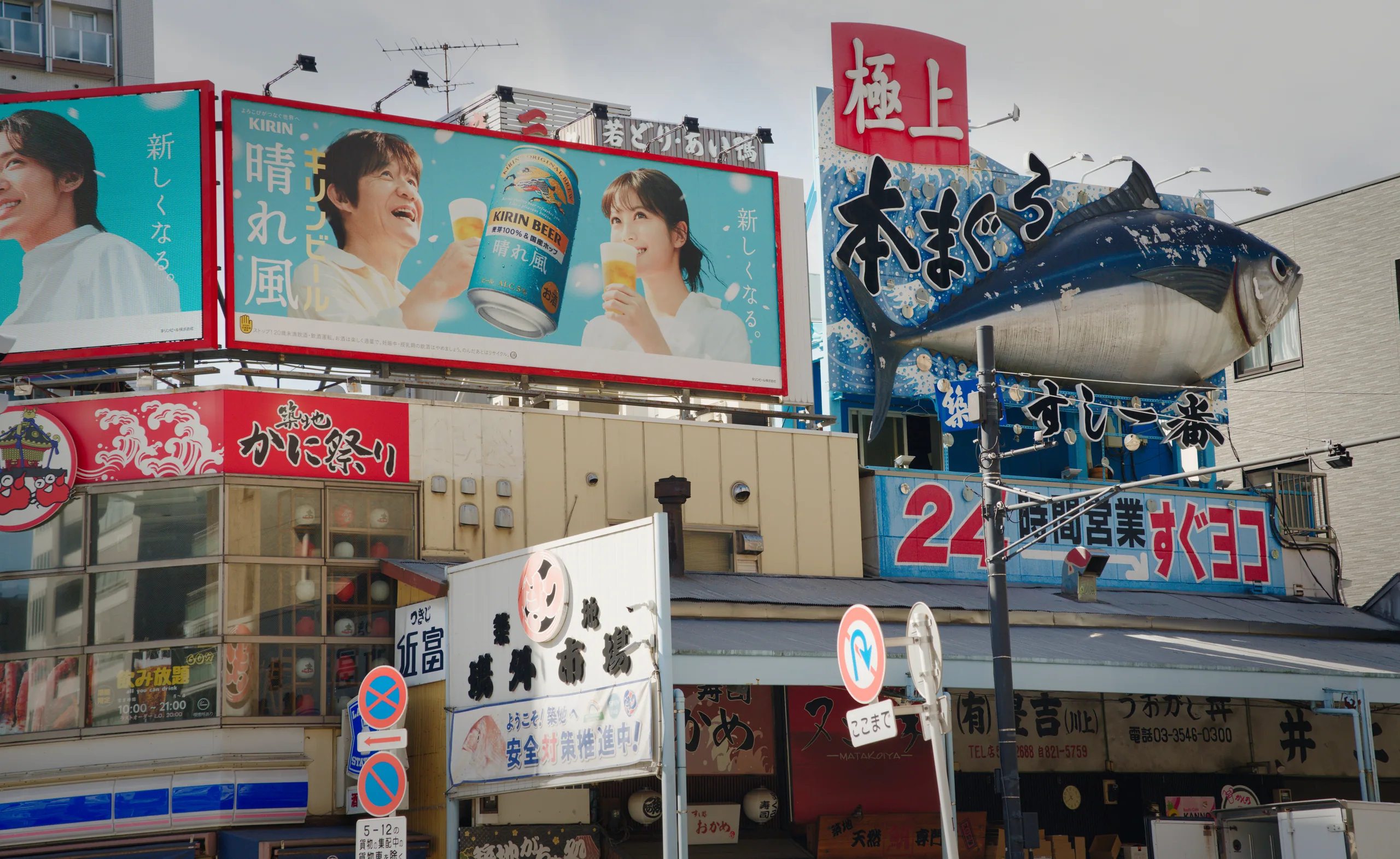 Storefronts and large advertising billboards line a busy shopping street with pedestrians and parked vehicles.