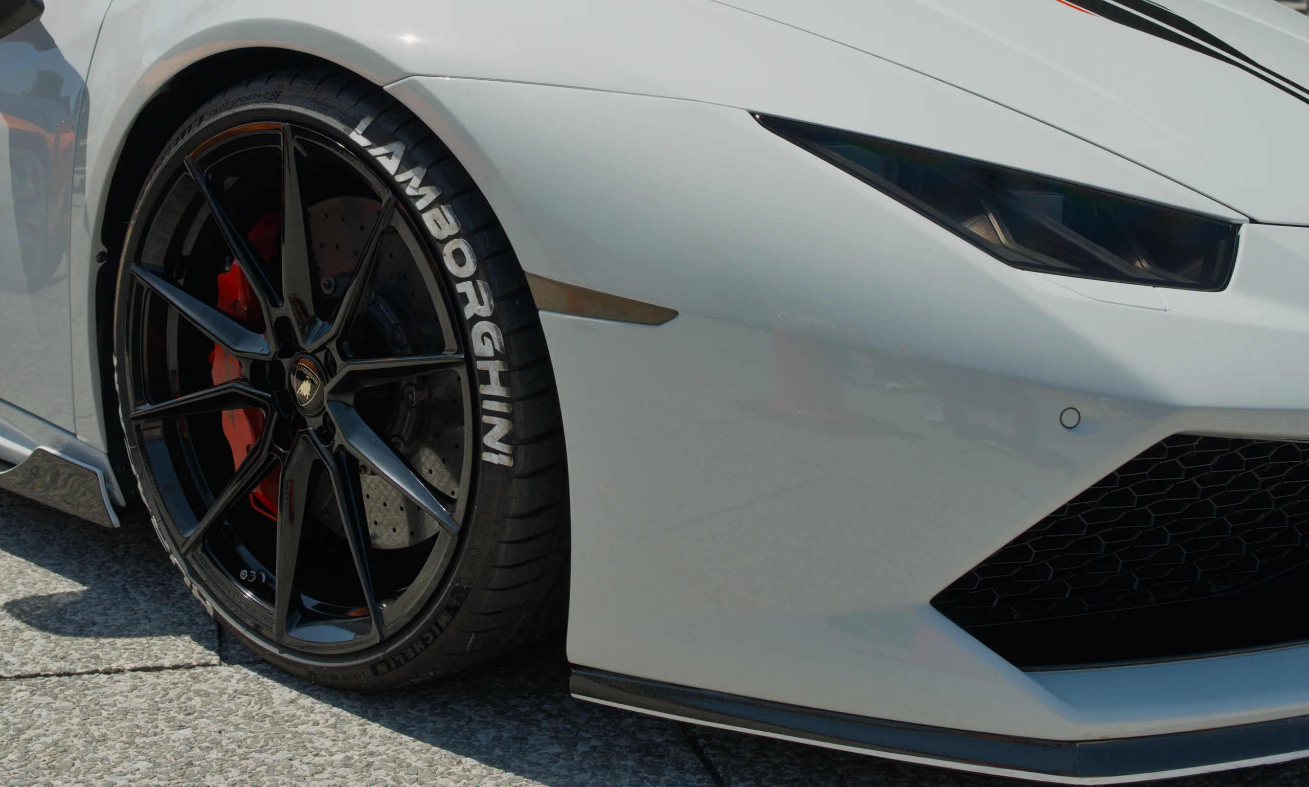 A white sports car's wheel and lower side panel, showing the tire and body detail.