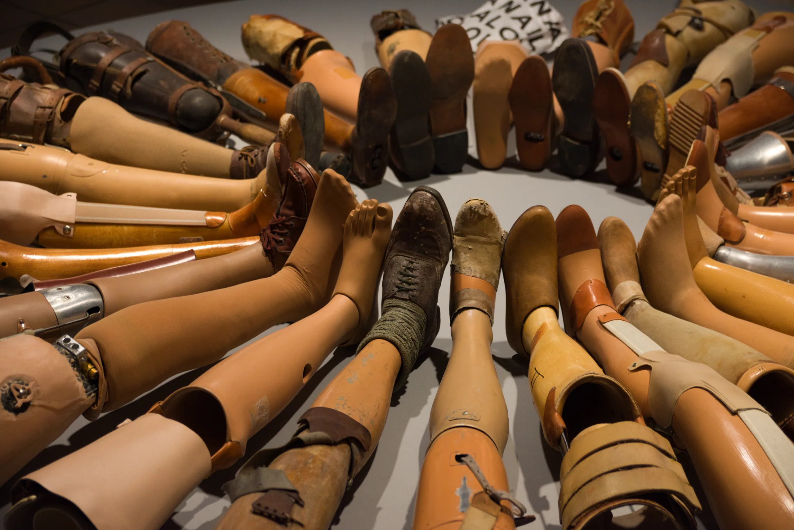 A museum display of dozens of prosthetic legs in wood, leather and metal, arranged in a dense circle.